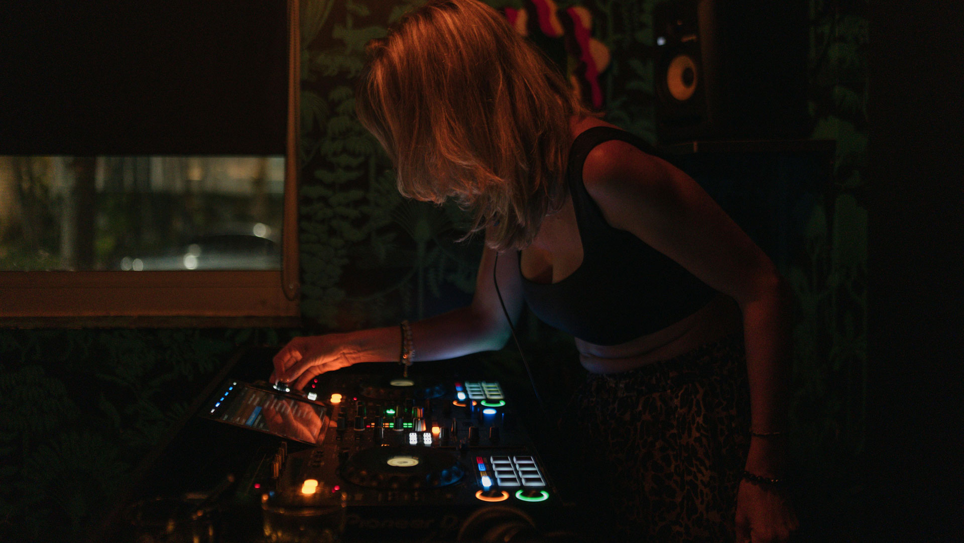 DJ mixing music on a dark nightclub stage with colourful lights.
