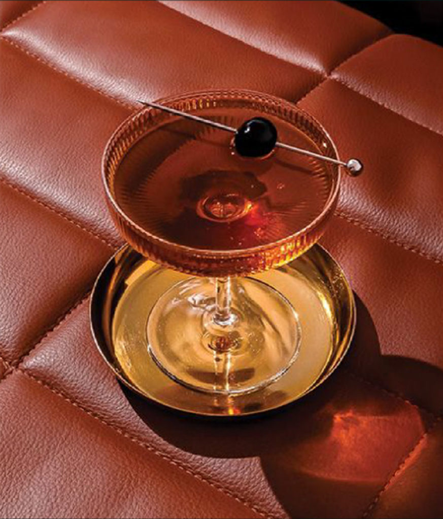 Elegant cocktail in a coupe glass with a cherry garnish, placed on a quilted brown leather surface.